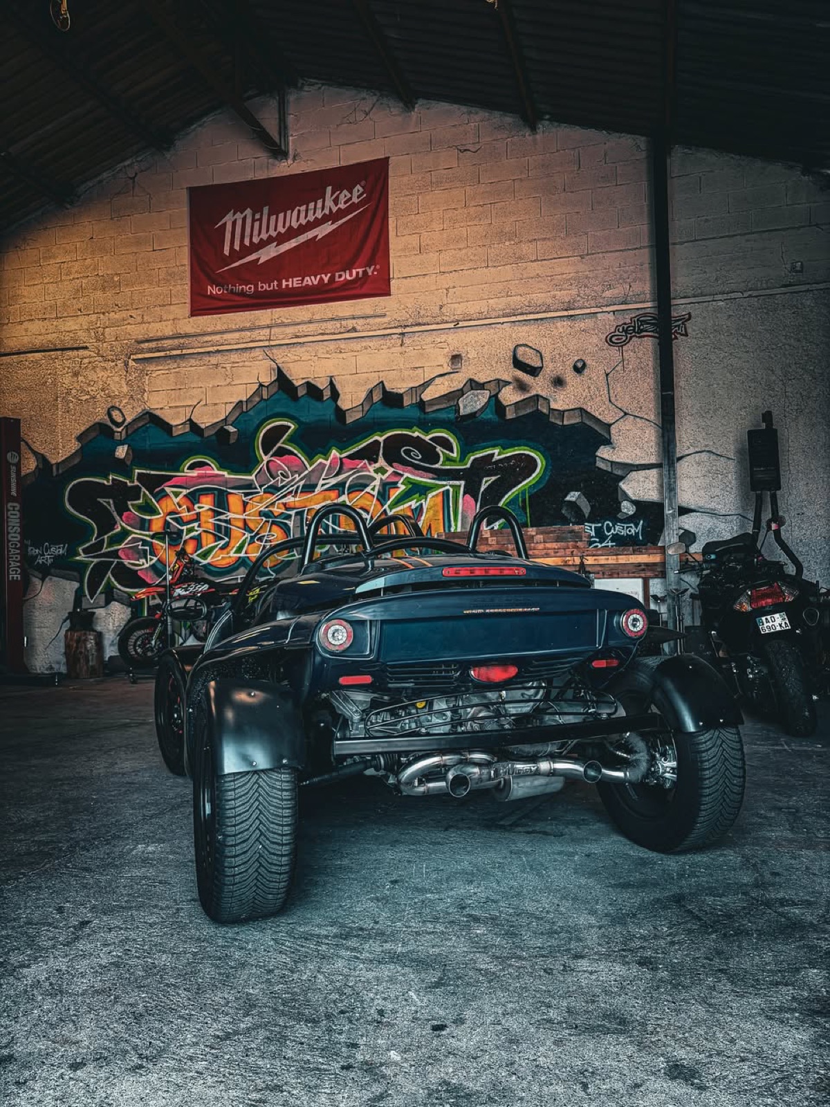 Voiture de piste type Caterham à l'atelier, ligne d'échappement visible sous caisse.